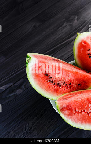 Hintergrund der drei Scheiben eine Wassermelone in eine weiße Platte auf einem schwarzen Holztisch Ansicht von oben. Leeren Raum für Text Stockfoto