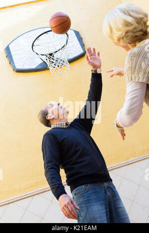 Lächelnd aktiv Reifes Paar spielen Basketball in Terrasse Stockfoto