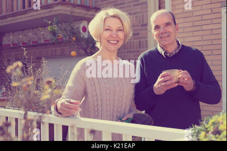 Paar außerhalb ihres Hauses auf einer Terrasse mit Garten Instrumente und eine Tasse heißen Getränk in den Ruhestand Stockfoto