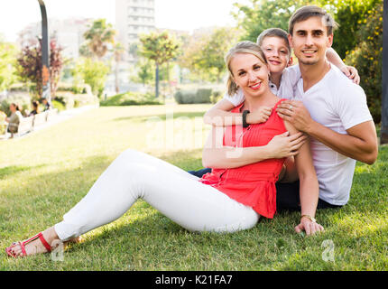 Junge glücklich Elternteil mit Junge im Teenager-Alter sitzen auf grünen Gras im Park Stockfoto