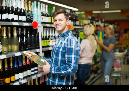 Positive lächelnden jungen Kerl Auswahl Flasche Wein im Supermarkt Stockfoto