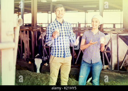 Porträt von zwei Happy farm workers Holding Glas mit Milch in der Nähe des Kuhstalls Stockfoto