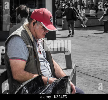 Mann sitzt auf der Bank mit Ohrhörer, Musik hören. Liverpool, England, UK Stockfoto