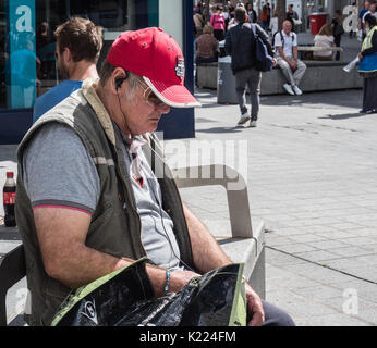 Mann sitzt auf der Bank mit Ohrhörer, Musik hören. Liverpool, England, UK Stockfoto