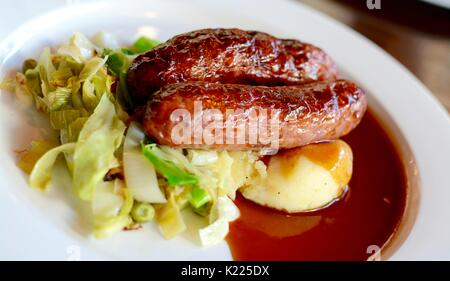 Würstchen und Kartoffelbrei mit saisonalen Gruenen mit Rotwein Soße auf einem weißen Teller serviert Stockfoto