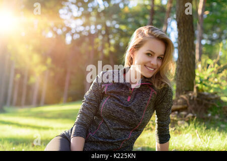 Attraktive lächelnde junge blonde Frau, tragen, Sportswear, Entspannung nach dem Training in einem Wald Stockfoto