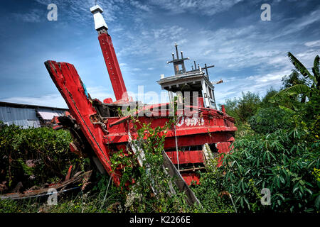 Verlassene und verfallende hölzerne Fischerboot zwischen Gras und Unkraut an Land. Thailand Südostasien. Stockfoto