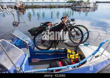 Taipalsaari, Finnland - Juli 2, 2015: Zwei Tourenräder sicher mit einem Fischerboot mit bunten Packtaschen auf dem Boot, gebunden durch den Saimaa-see, F Stockfoto