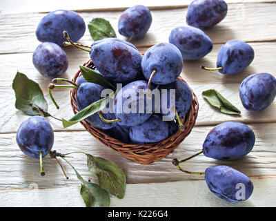 Pflaumen Früchte nützliche Diätetische große Frische frische Ernte saftiges Schöne süße liegen in einem Weidenkorb und auf einer hölzernen Hintergrund mit grünen Blättern Stockfoto