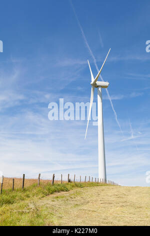 Windenergieanlage auf einem Hügel in einer frisch geernteten agricutltural Feld mit einem rustikalen hölzernen Zaun in einem Konzept der natürlichen Ressourcen und der erneuerbaren Energien. Stockfoto