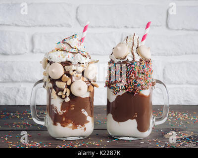 Nahaufnahme von zwei Freakshake im Einmachglas auf braunen Tisch. Ausgeflippt Milchshake mit Schokolade, Keks Kekse und Zucker bestreuen. Trendige Lebensmittel conce Stockfoto