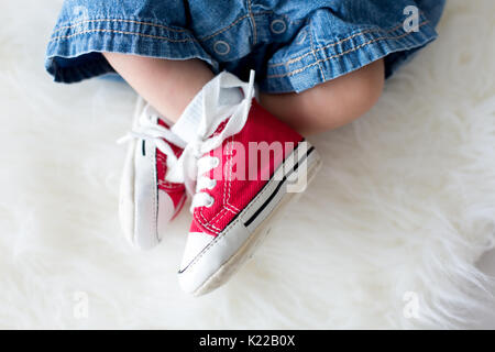 Modischen roten Sneakers auf dem kleinen neugeborenen Baby jungen Füße, baby boy Jeans und Turnschuhe Stockfoto