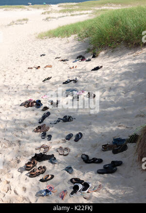 Sandalen, Flip Flops und Schuhe in den Sand links von barfuß Beachgoers. Stockfoto