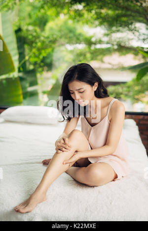 Asiatische Frau sitzt auf dem Bett mit den Beinen verletzt. Stockfoto