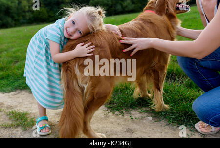 Adorable kleine blonde Mädchen lächelnd und ihres süßen Hund golden retriever umarmen Stockfoto