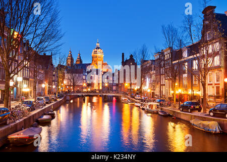 Ein Kanal im Rotlichtviertel in Amsterdam, Die Niederlande mit der St. Nikolaus Kirche am Ende fotografiert in der Nacht. Stockfoto