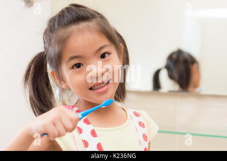 Süße niedliche kleine Kinder Mädchen im Badezimmer mit zahnbürste Reinigung der Zähne, indem sie sich mit Spiegel Reflexion Bild Hintergrund zu Hause lernen. Stockfoto