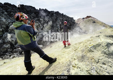 Zwei junge Frauen, die Touristen auf dem Smartphone auf dem Hintergrund von Schwefel fumarolenfeld fotografiert im Krater des Avachinsky Vulkan auf Kamtschatka. Stockfoto