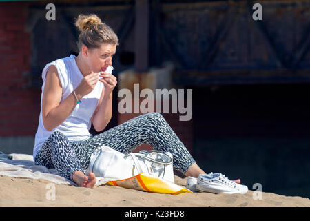 Lytham St Annes on Sea, Lancashire. Wetter in Großbritannien. August 2017. Sitzende Frau rollt an einem heiß-sonnigen Tag an der Fylde-Küste mit Zigarette, da die versprochene Hitzewelle am frühen Nachmittag eintrifft. Urlauber, Familien strömen zum Strand, um die versprochene Sonne zu genießen. Stockfoto