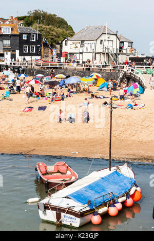 England, Viking Bay, Broadstairs. Strand total vollgepackt mit Sun Asylbewerber während der heißen Wetter. Der Strand und das Meer im Blick, Massen von Menschen am Strand. Strahlender Sonnenschein. Angeln Boot im Vordergrund und das Wahrzeichen der alten Rettungsboot das Weiße Haus im Hintergrund. Stockfoto