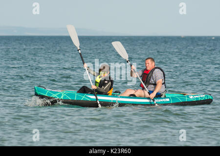 Mann und Junge paddeln im aufblasbaren Kajak auf dem Meer, Dorset, Großbritannien Stockfoto