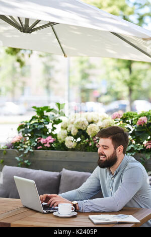 Lächelnd bärtigen Geschäftsmann Arbeiten im Café im Freien Stockfoto