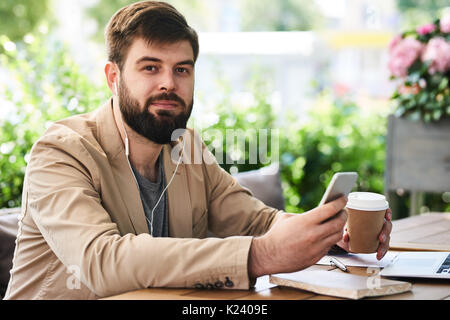 Lächelnd bärtiger Mann mit Smartphone im Cafe Stockfoto