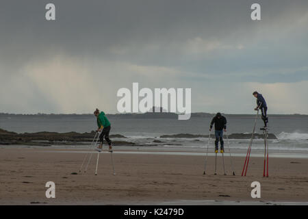 Drei stelzende Wanderer in der Praxis am Strand in Northumberland, wenn Regen naht und mit Bamburgh Castle im Hintergrund Stockfoto