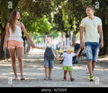 Die europäische Familie mit zwei kleinen Kindern gehen im Park an einem sonnigen Tag Stockfoto