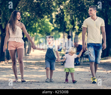 Die europäische Familie mit zwei kleinen Kindern gehen im Park an einem sonnigen Tag Stockfoto