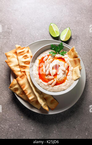 Hummus von weißen Bohnen mit würzigen Öl der Hot Pepper und hausgemachte knusprige Brote auf einem grauen Stein Tabelle Stockfoto