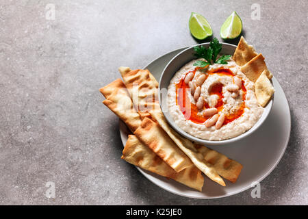 Hummus von weißen Bohnen mit würzigen Öl der Hot Pepper und hausgemachte knusprige Brote auf einem grauen Stein Tabelle Stockfoto