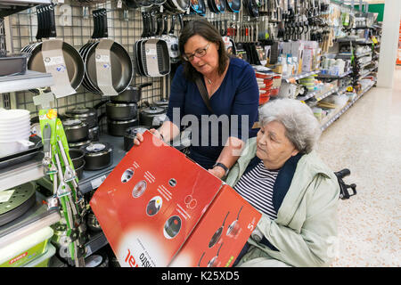 Pflegeperson oder Assistent hilft, eine ältere Frau in einem Rollstuhl einige neue Töpfe in einem Supermarkt. Stockfoto