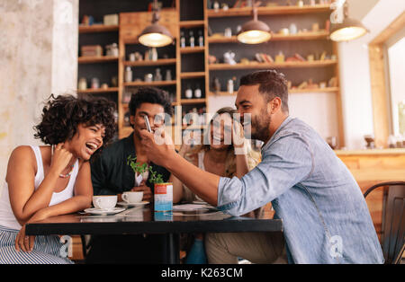 Junge Gruppe von Freunden in einem Cafe sitzen und über Handy. Junge Männer und Frauen im Cafe sitzen und Lachen. Stockfoto
