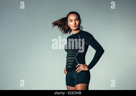 Portrait von Fitness Frau in Langarm-T-Shirt stand mit den Händen auf den Hüften. Weibliche Modell tragen Fitnessraum Kompression t-shirt über grauen Hintergrund. Stockfoto