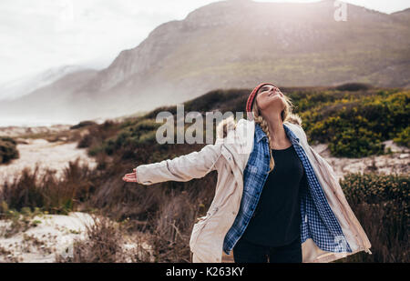 Schöne junge Frau mit einem Winter Tag am Strand. Fröhliche Frau stehend auf einem kalten Winter Strand mit ihren ausgestreckten Armen und ihre Augen schließen Stockfoto
