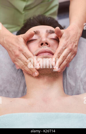 Junger Mann das Gesicht massiert. Hände der Masseurin arbeiten. Stockfoto