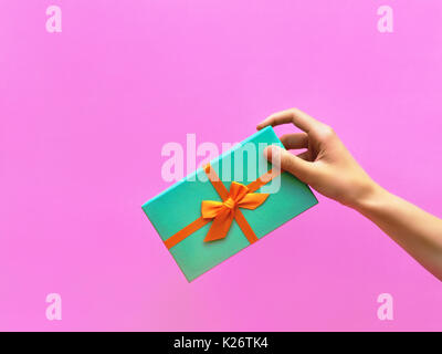 Geschenkbox trendy gestylt Foto weibliche Hand ein Geschenk Box gegen eine lila wand hintergrund Front View modern pop art Foto mit Platz für Text Stockfoto