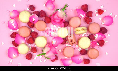 Petit Fours overhead Präsentation der Macarons und Meringues mit Beeren und Rosenblätter auf rosa Holz Tabelle Tabelle. Stockfoto