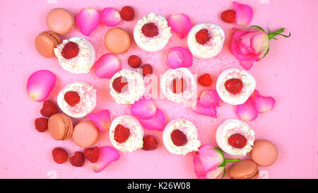 Petit Fours overhead Präsentation der Macarons und Meringues mit Beeren und Rosenblätter auf rosa Holz Tabelle Tabelle. Stockfoto