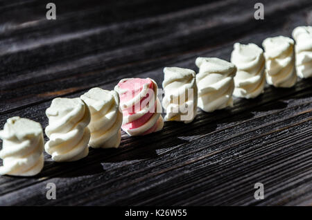 Weiß und rosa Marshmallows ordentlich in einer Reihe auf einem schwarzen Holztisch angeordnet. Frisch und süßen Marshmallows Hintergrund Stockfoto
