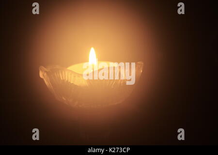 Ein Teelicht mit einer kleinen Flamme auf schwarzem Hintergrund Stockfoto