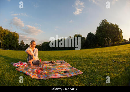 Eine Frau mittleren Alters allein auf eine Wolldecke, wie die Sonne Stockfoto