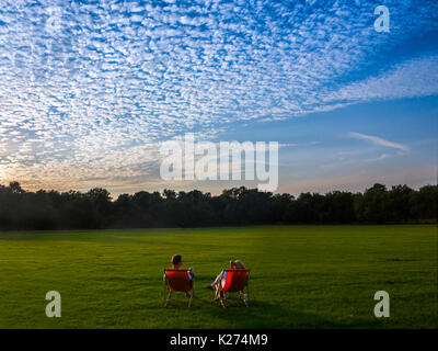 Ein paar Sommern Abend genießen können, sitzen in Liegestühlen in einem Londoner Park Stockfoto