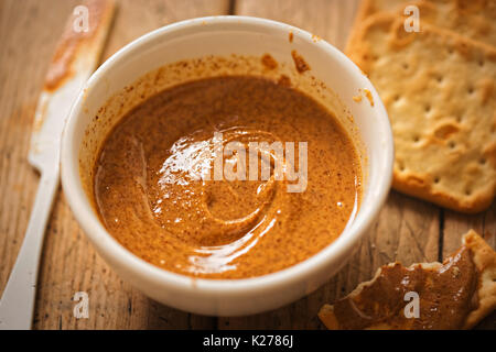 Almond Butter in Schüssel mit Crackern auf hölzernen Tisch Stockfoto