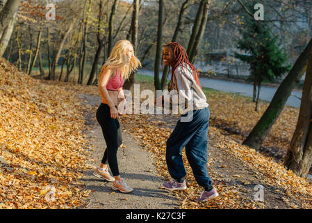 Mädchen Spaß in autamn Park nach dem Joggen. Blond und afrikanische Frauen lächeln Stockfoto