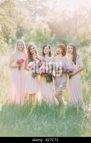 Die Gruppe Foto der Braut und Brautjungfern Holding die Riesige rosa Blumensträuße in der Mitte des sonnigen grünen Wald. Stockfoto