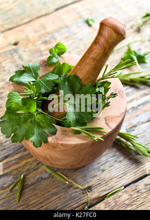 Verschiedene Kräuter auf einem alten Holztisch. Holz- Mörtel mit Rosmarin, Koriander, Thymian und Petersilie. Stockfoto