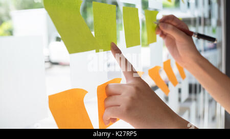 Hand mit Post-it Haftnotiz mit Brainstorming auf Papier. Stockfoto