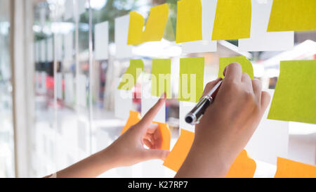 Hand mit Post-it Haftnotiz mit Brainstorming auf Papier. Stockfoto